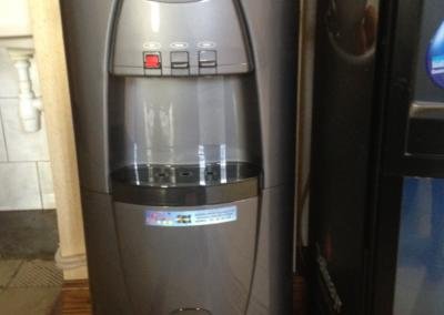 Szary dystrybutor wody obok automatu do kawy